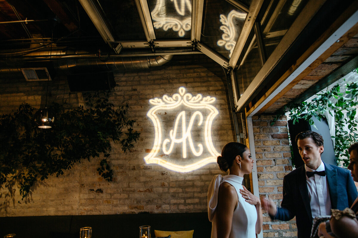 A light shining the bride and groom's initials on white brick wall of Ada Restaurant