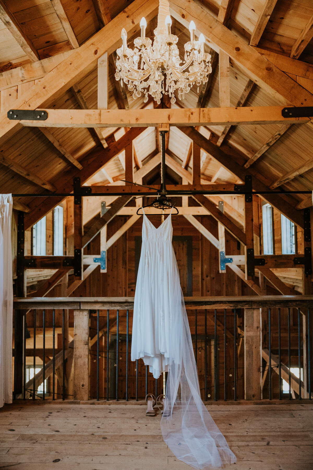 Wedding dress hangs off of rafters in large warm barn.
