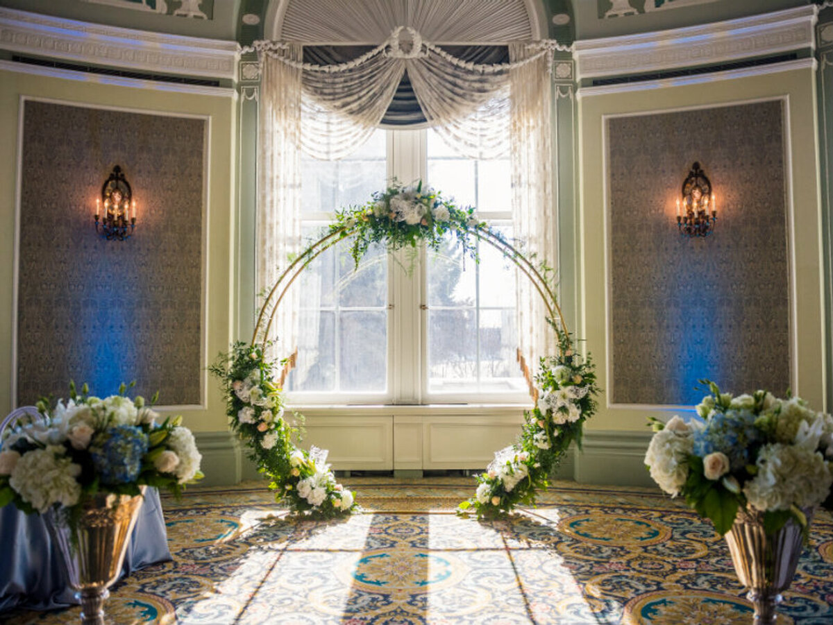 Beautiful indoor ceremony with gold hoop backdrop, and elegant white florals, at The Fairmont Hotel, classic and experienced, Edmonton wedding venue, featured on the Brontë Bride Vendor Guide.