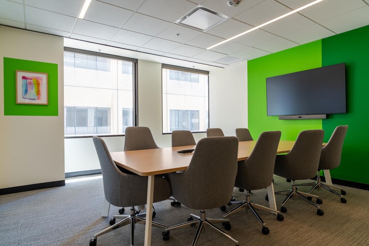 Conference room with bright green accent wall and grey swivel chairs around a long wood table.