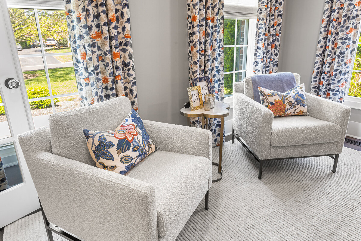 two grey chairs with orange and blue accent pillows and drapes behind