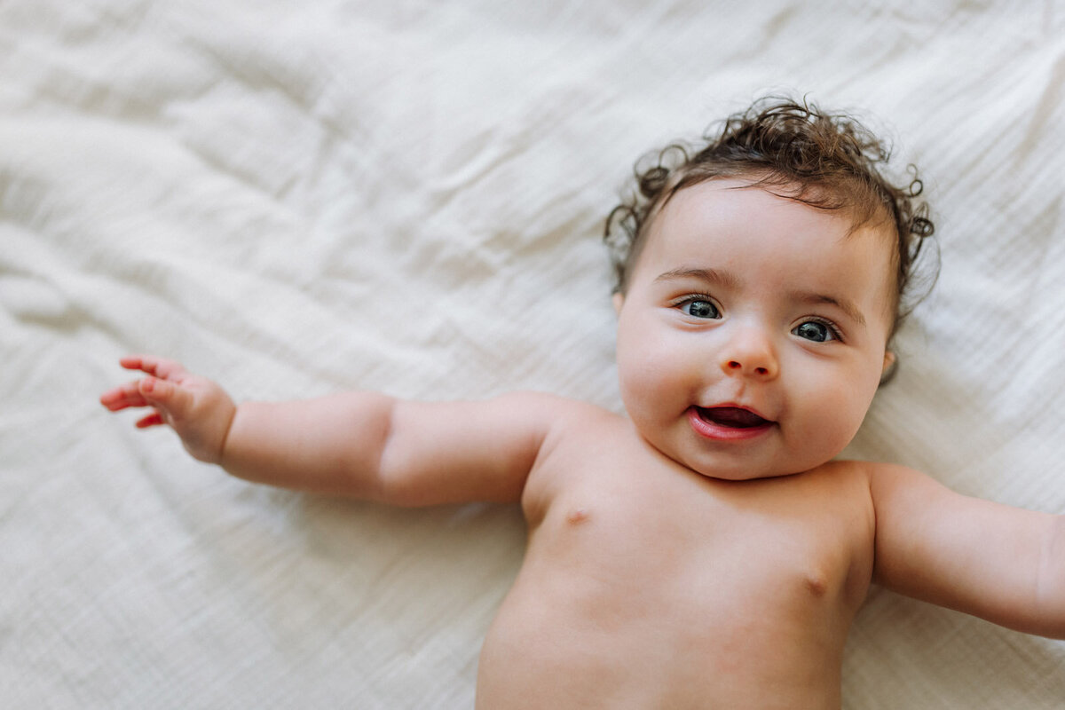 smiling baby in just a diaper laying on a blanket at home looking at the camera