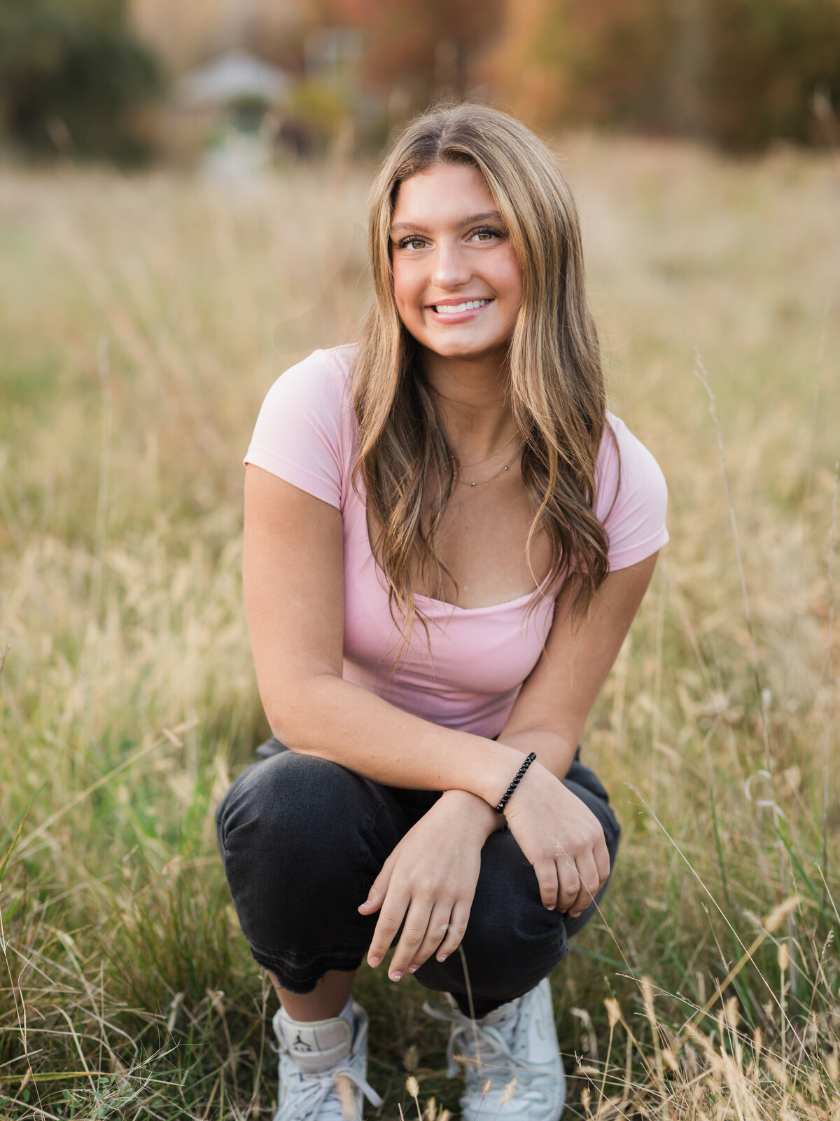 senior girl in pink top posing for senior photos in field Cleveland senior photographer