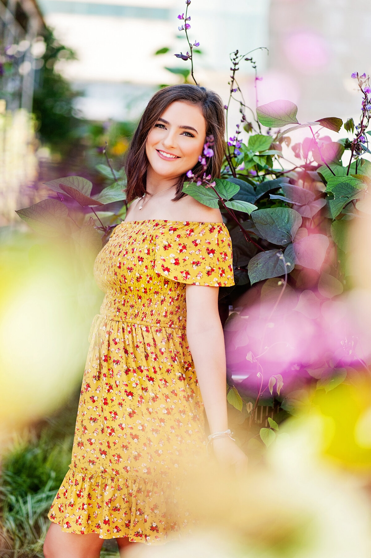 Mechanicsville high school senior girl poses wearing yellow floral dress in front of flowers at VMFA in Richmond, VA.