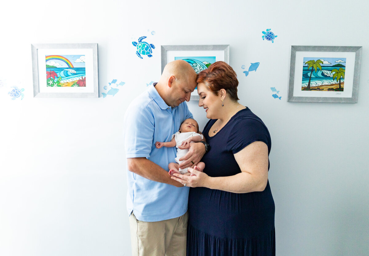 mom and dad holding newborn boy in a blue room with pictures of ocean