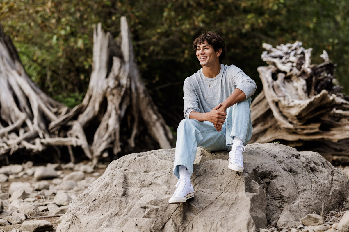 Young man sitting on a big rock smiling.
