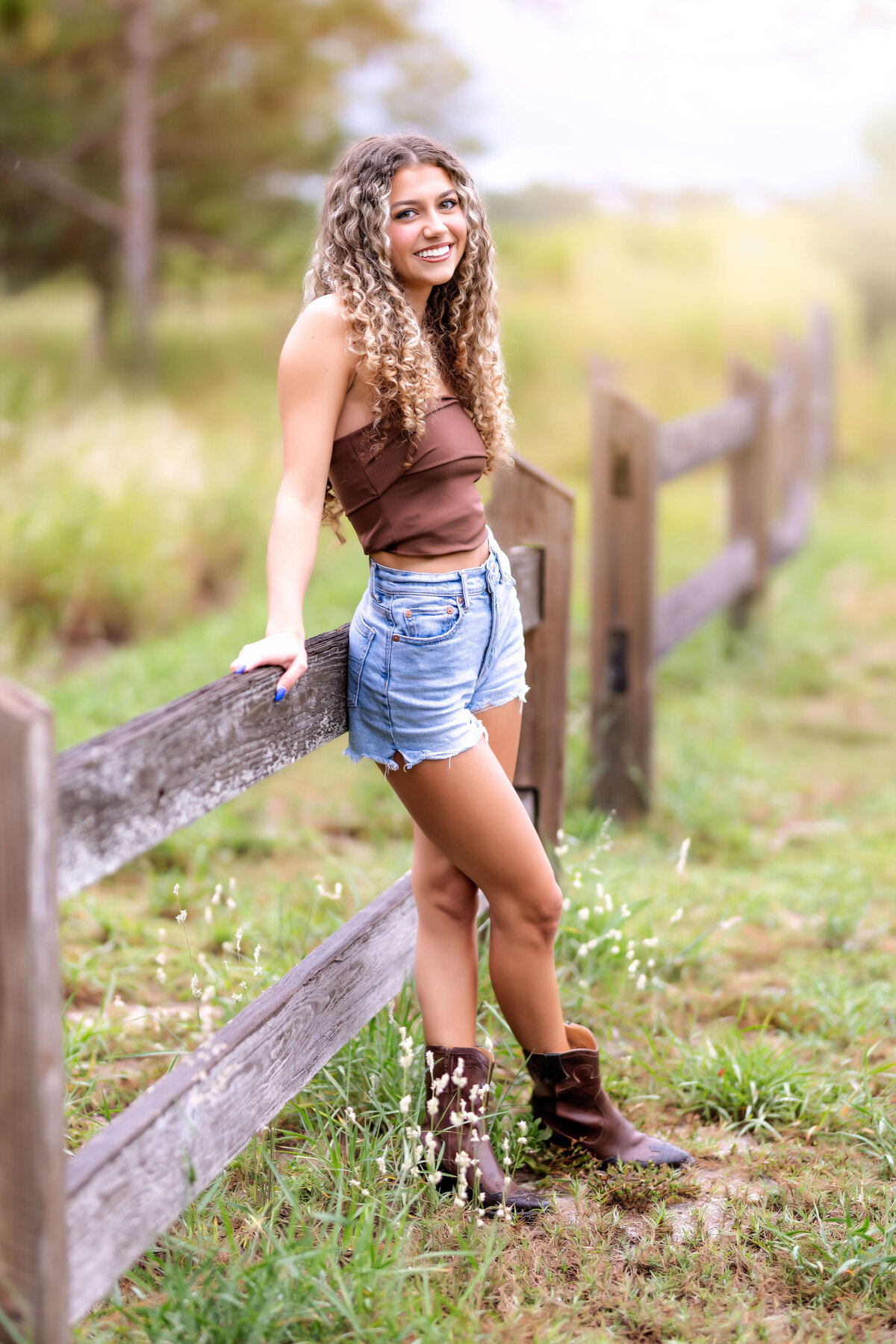 Senior girl leaning casually against a rustic fence at sunset during her Orlando senior photography session.
