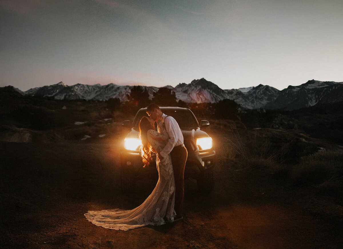 A bride and groom kiss at dusk, while in the light of their Toyota truck headlights, while on their wedding day in Mammoth Lakes. 