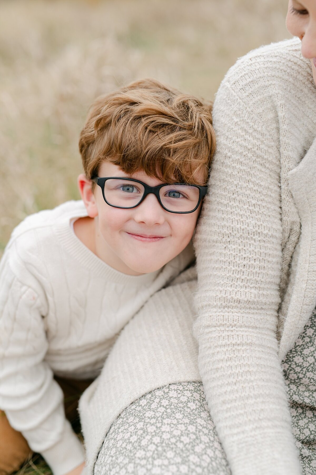 Boy smiling at camera while leaning against his mom