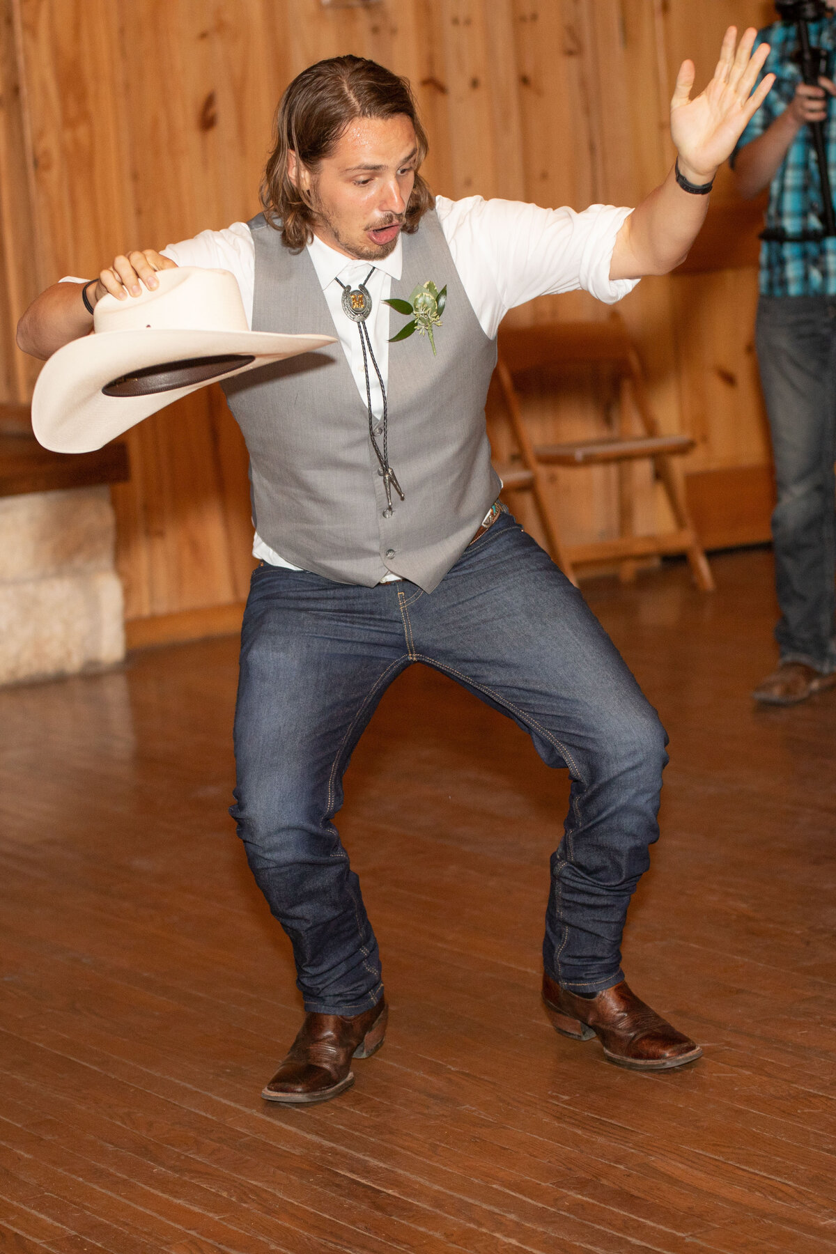 wedding guest holds cowboy hat while dancing in gray vest