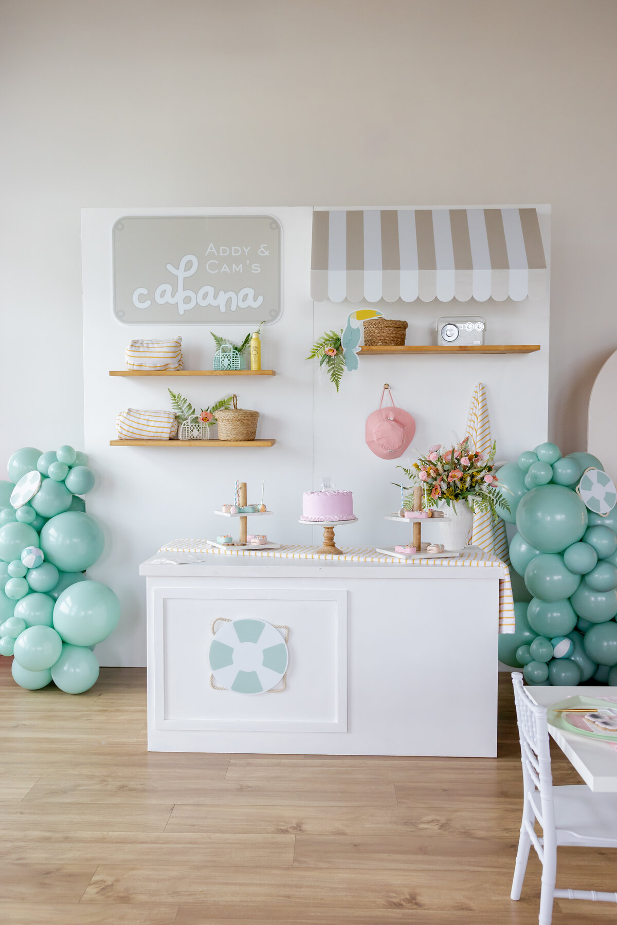 Decorated wall for a beach party with toucans, flowers and desserts.