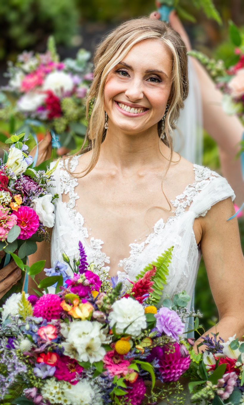 A bride with blonde hair smiles while surrounded with flowers