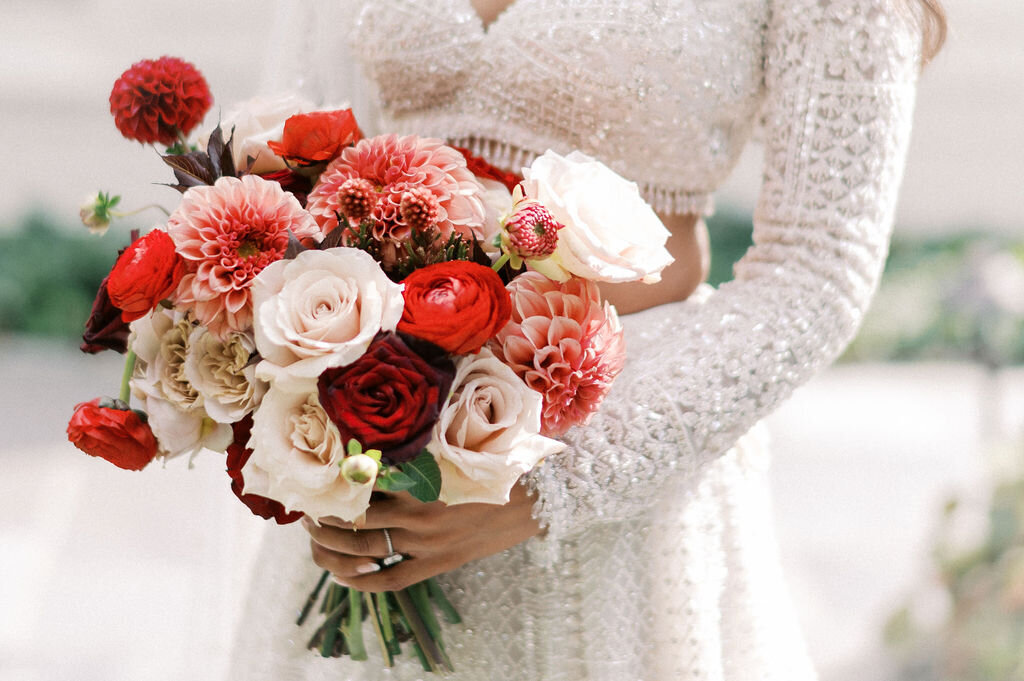 Close-up of a bridal bouquet featuring red dahlias, ranunculus, and blush roses at a wedding at Old Edwards Inn.