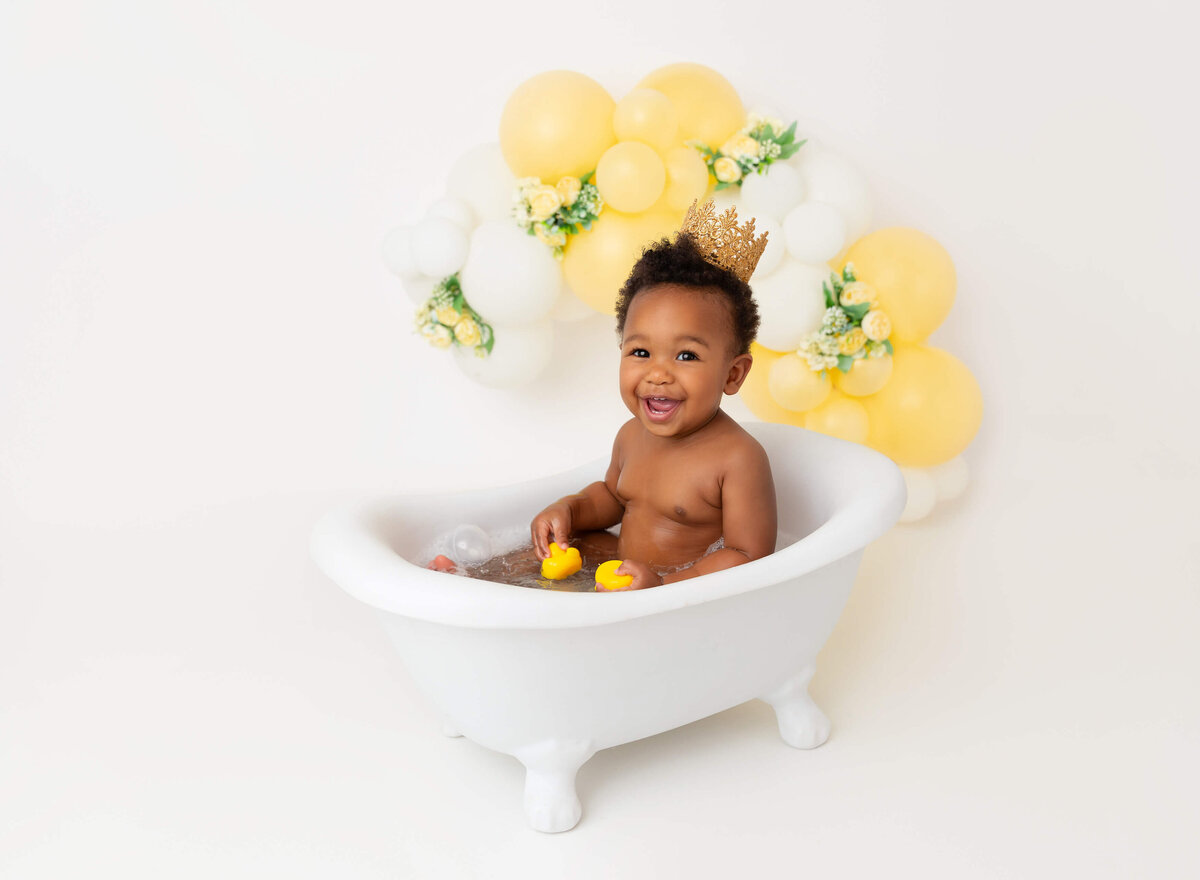baby girl playing in a white tub  for her yellow and white cake smash session  NYC