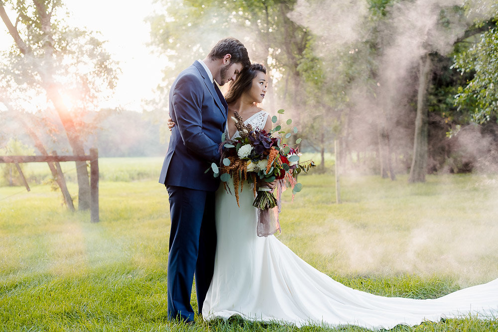 A couple stands intimately close together while the man looks down and the woman looks off into the distance