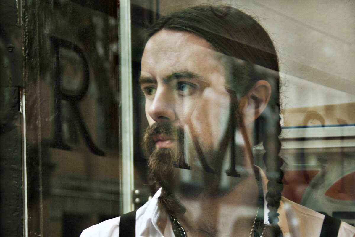 Musician Portrait closeup Matt Rose looking through window reflections of words across his face Reflections Gallery