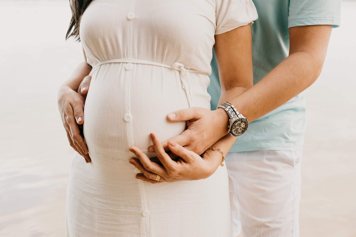 Crop pregnant woman embracing tummy with husband