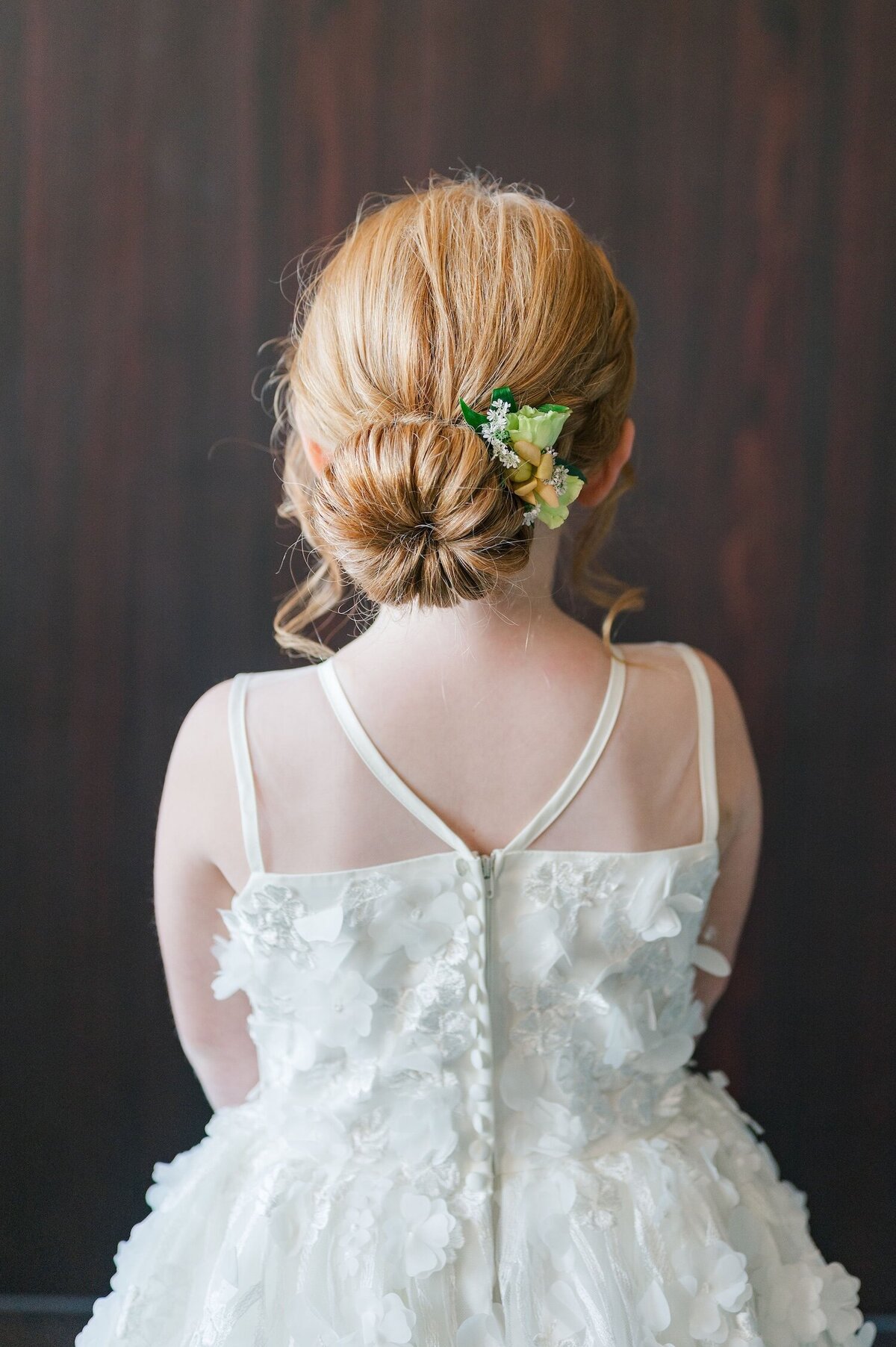 A flower girl wears her hair in a bun with florals popping out