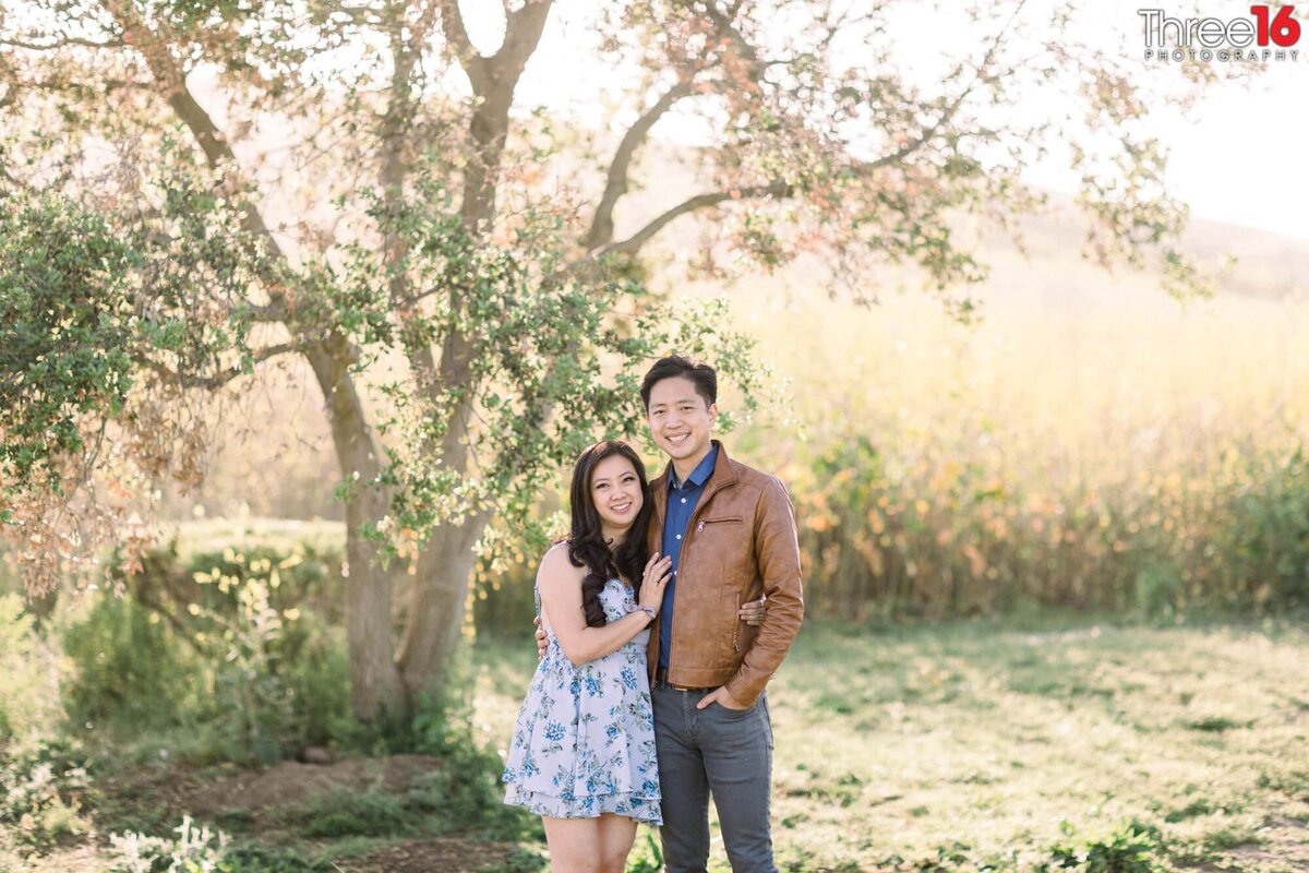 Engaged couple pose next to each other under a tree