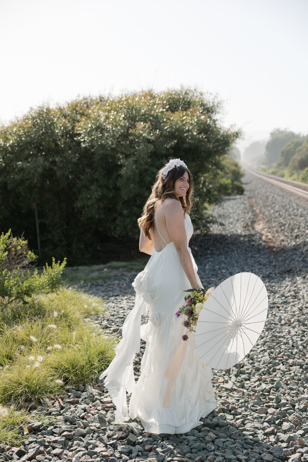 Glowing sunset solo bridal portrait of the bride walking away with a parasol at her La Jolla wedding in San Diego, California.