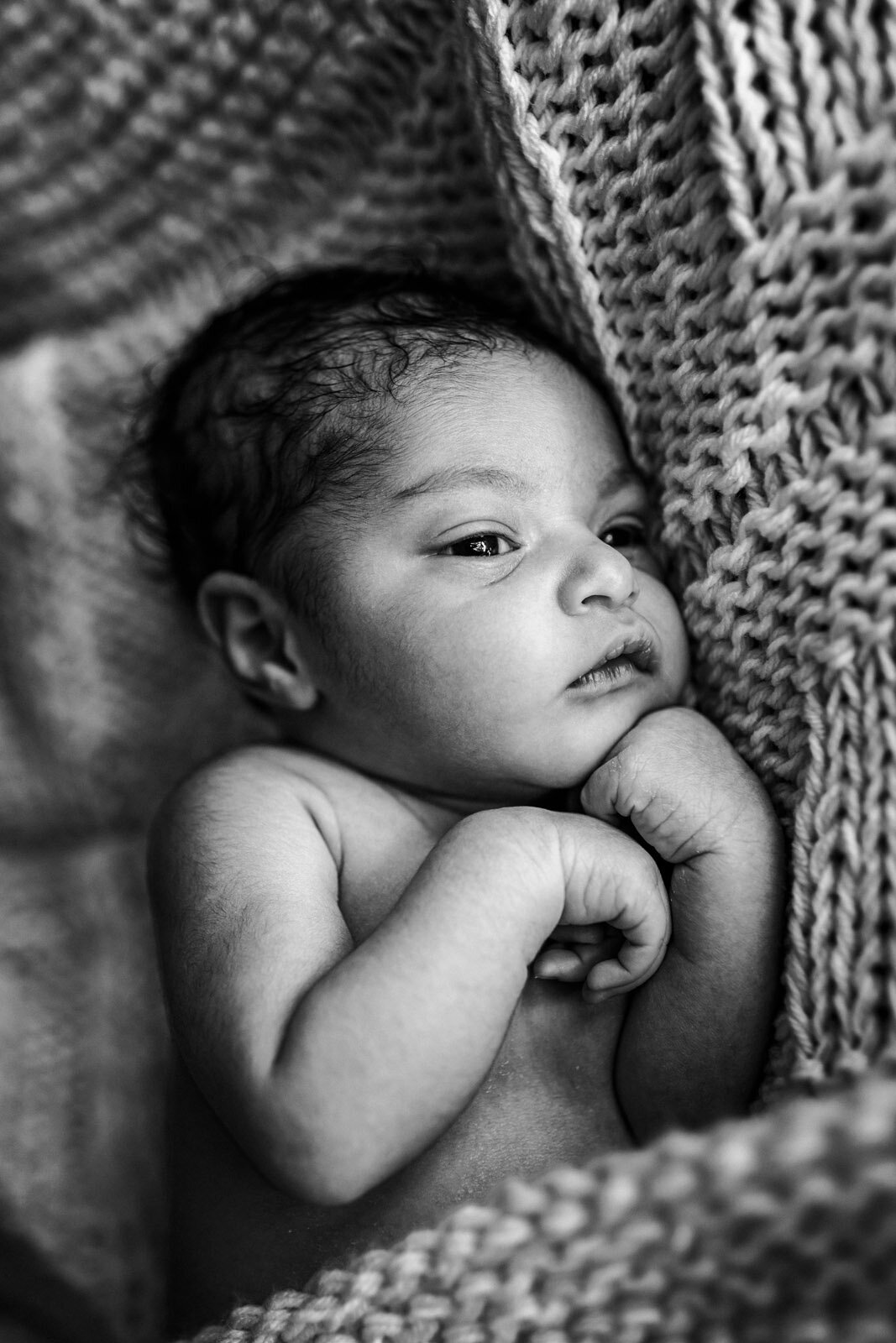 newborn with eyes open hands tucked up by face covered by blanket