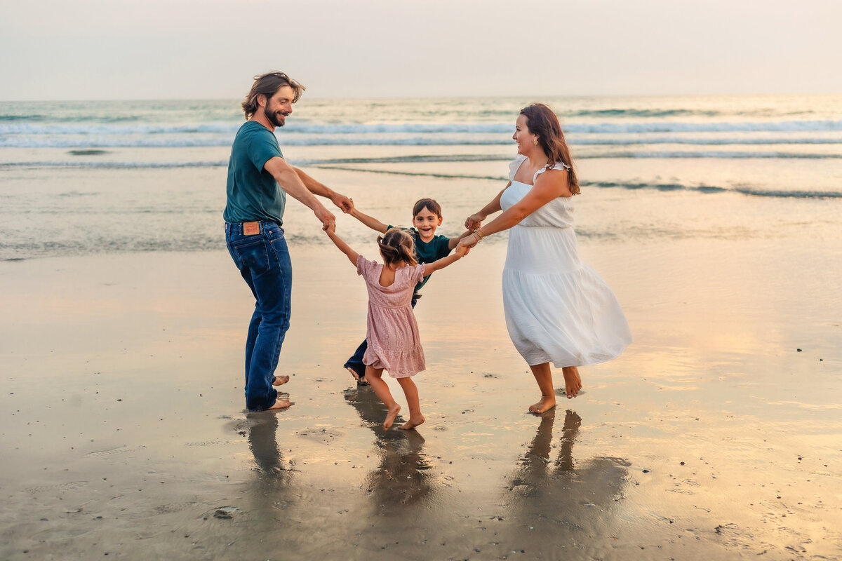 Family Photographer, a family of four hold hands and dance in a circle at the beach
