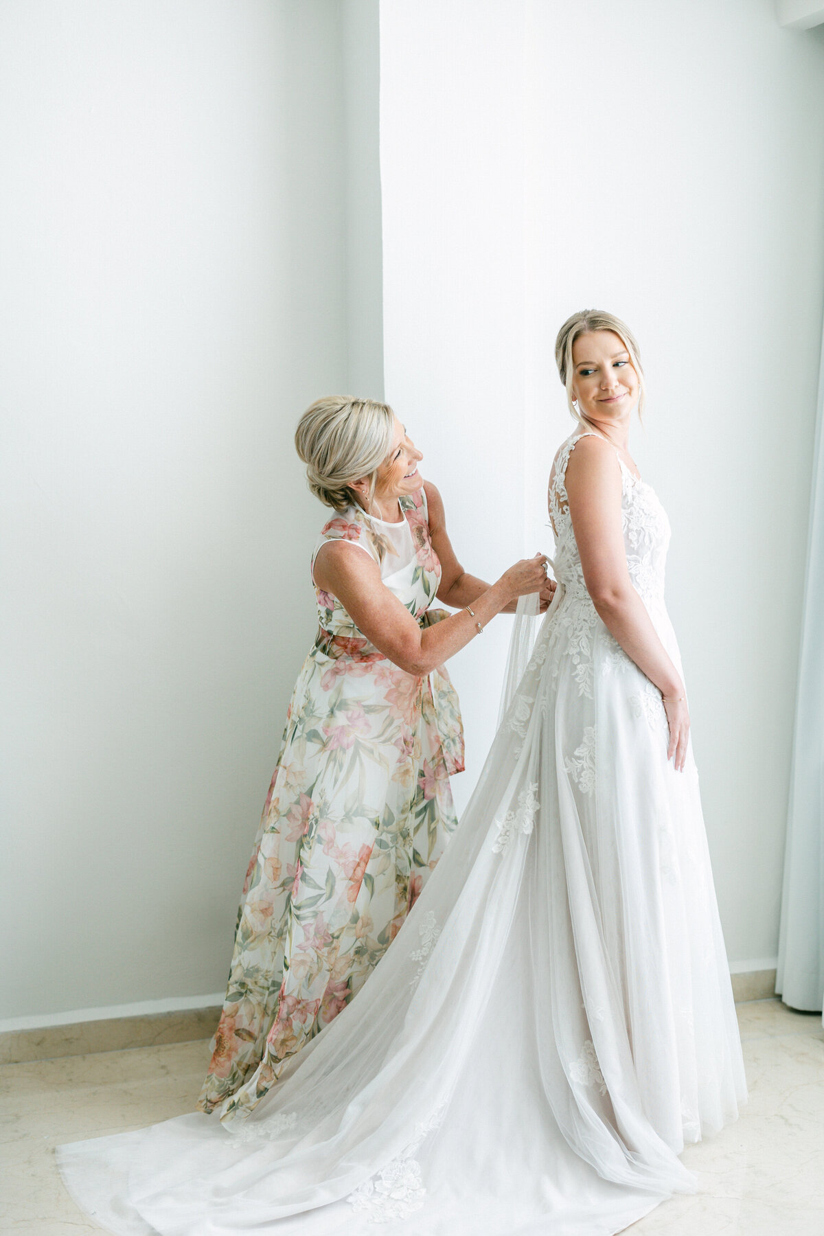 Bride’s mom helping with wedding dress buttons in bright Cancun suite, captured by Philadelphia wedding photographer.