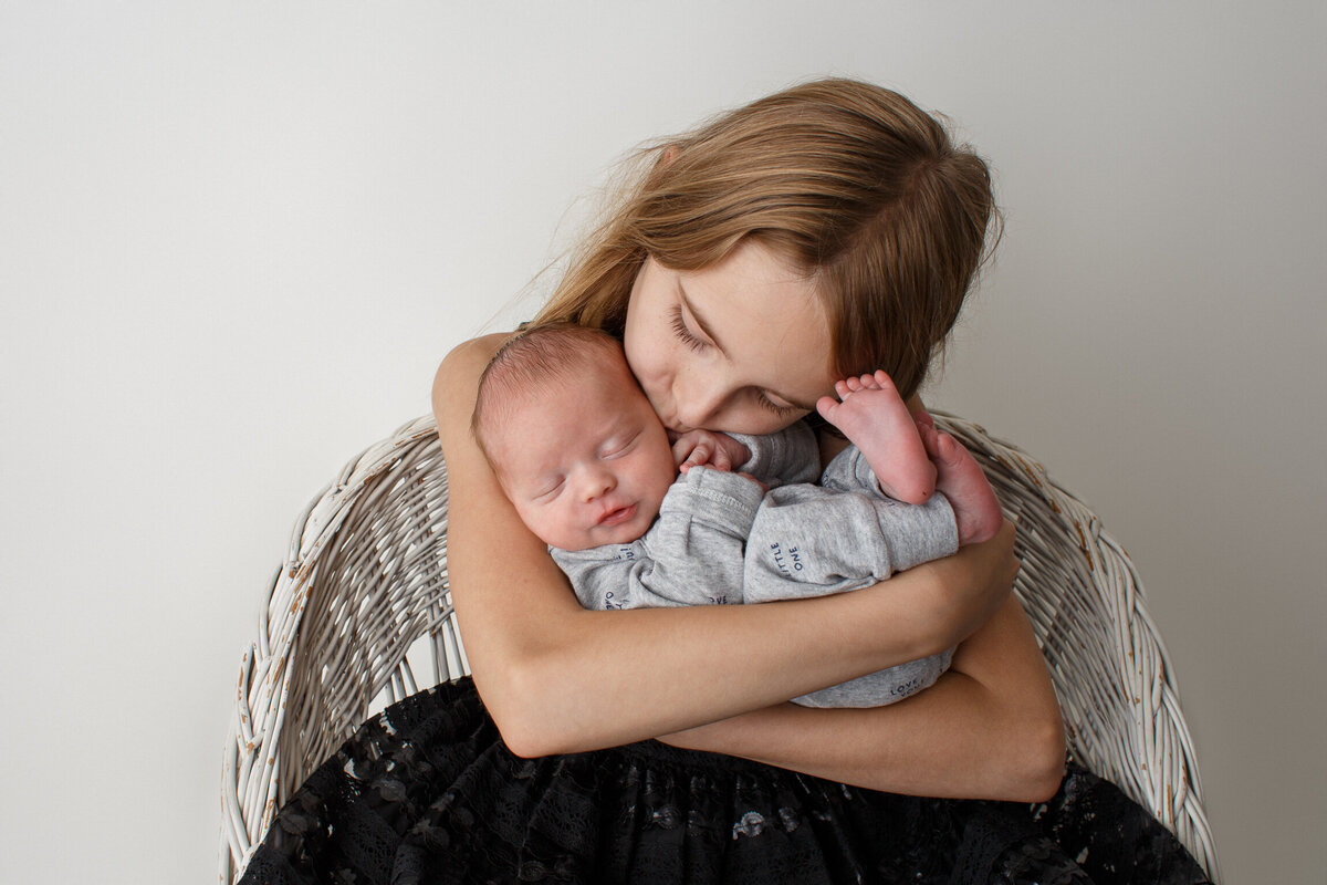 Young girl cradling her new baby brother in her arms and kissing him