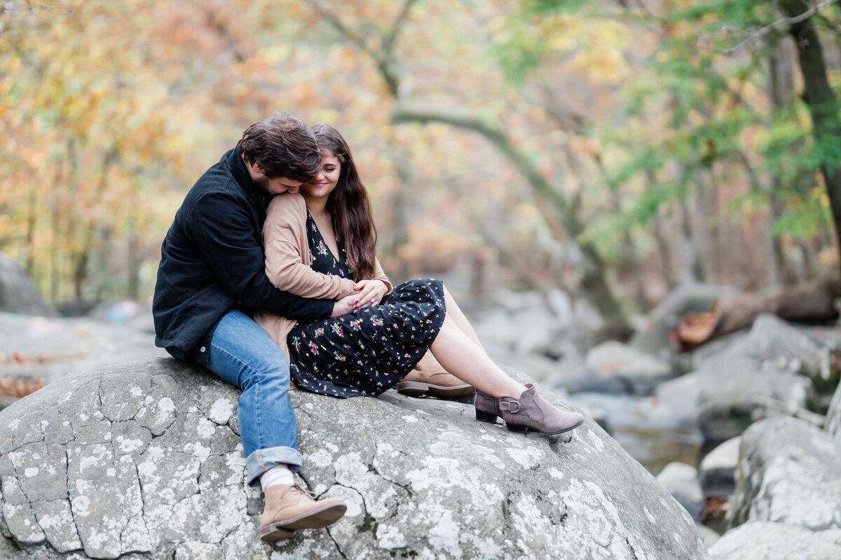 Couple hugging sitting on a rock in the middle of a river in the fall