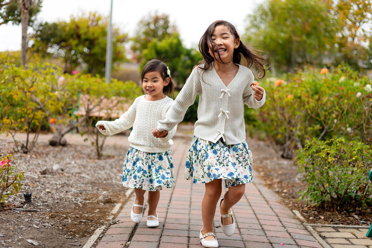 Two sisters running along a garden path in San Jose during outdoor Bay Area school photography lifestyle shoot – Ellobelle Photography