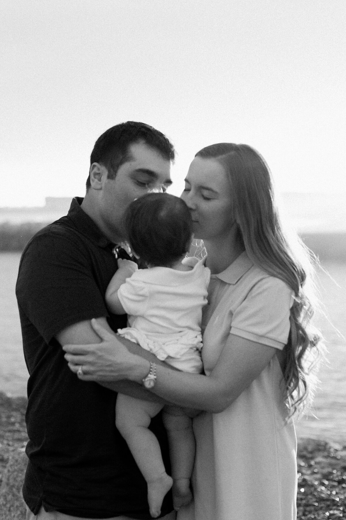Couple embrace their child on the beach in Maine.