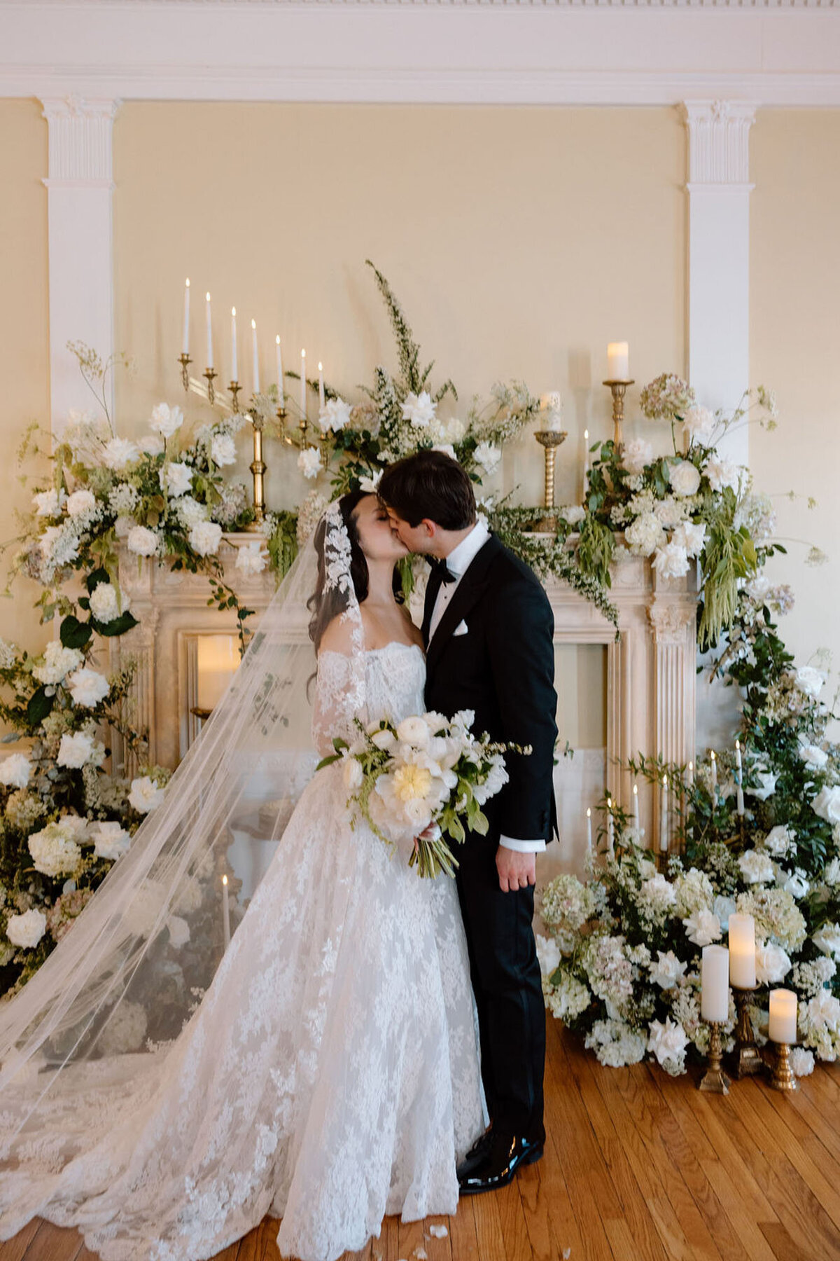 Bride and groom kissing in front of floral fireplace altar