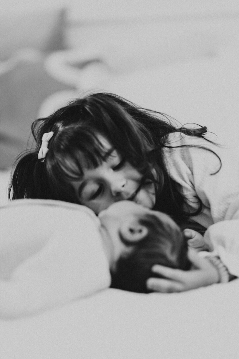 Petite fille allongée caressant la tête de son petit frère. Scène immortalisée en noir et blanc lors d'un shooting photo au studio.