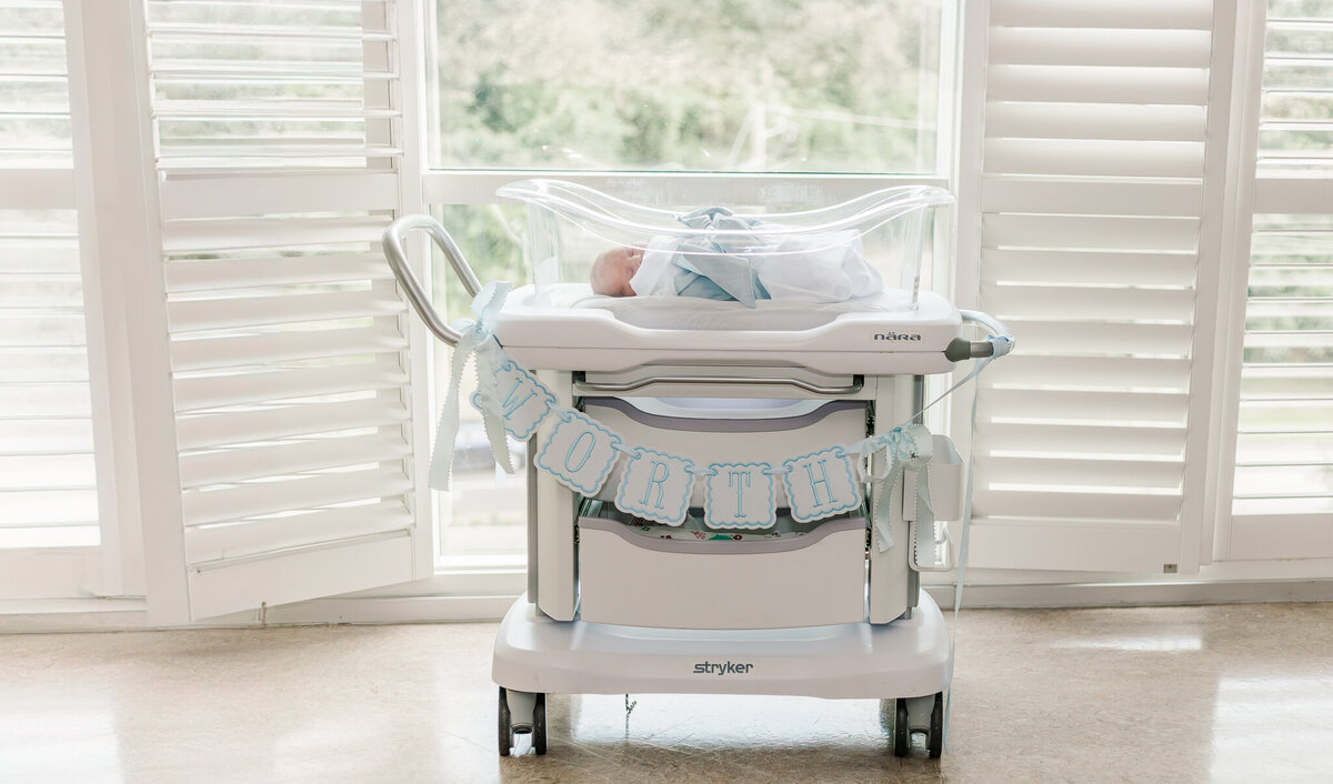 picture of baby boy wrapped in white swaddle in front of windows during fresh 48 photo session at Brookwood Hospital