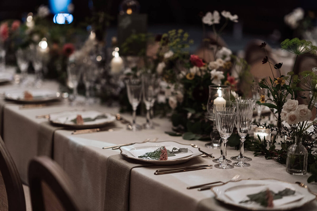 closeup of a long candlelit dining table with beige linen and flowers including cosmos and dahlias along the centre of the table in the nomad hotel london