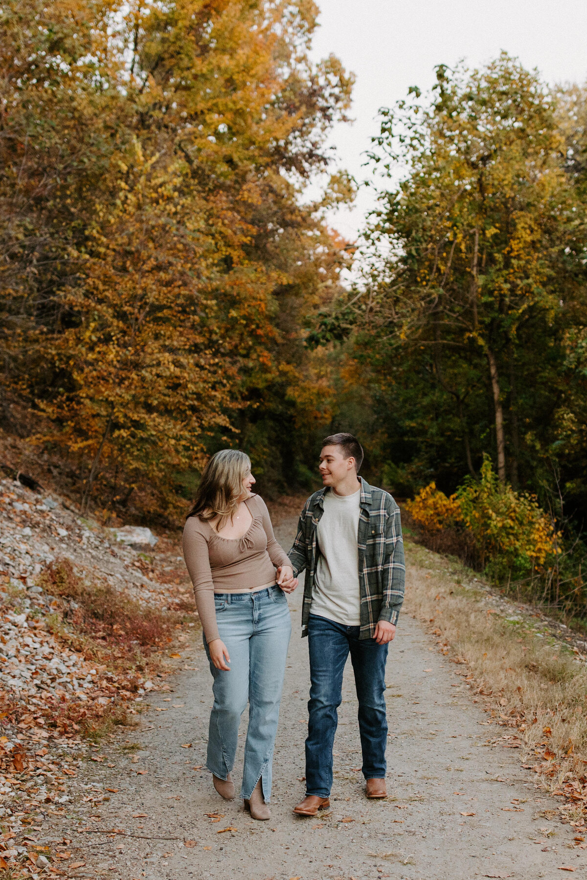 couple holding hands and looking at each other as they walk along a path
