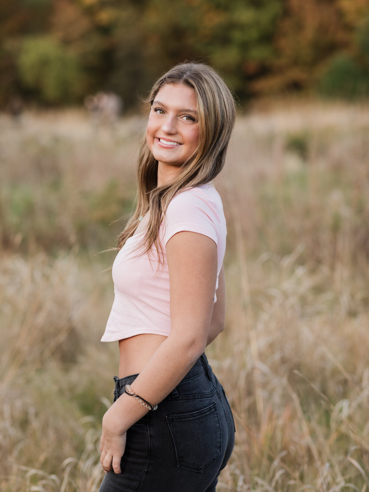 senior girl in pink top posing for senior photos in field cleveland senior photographer