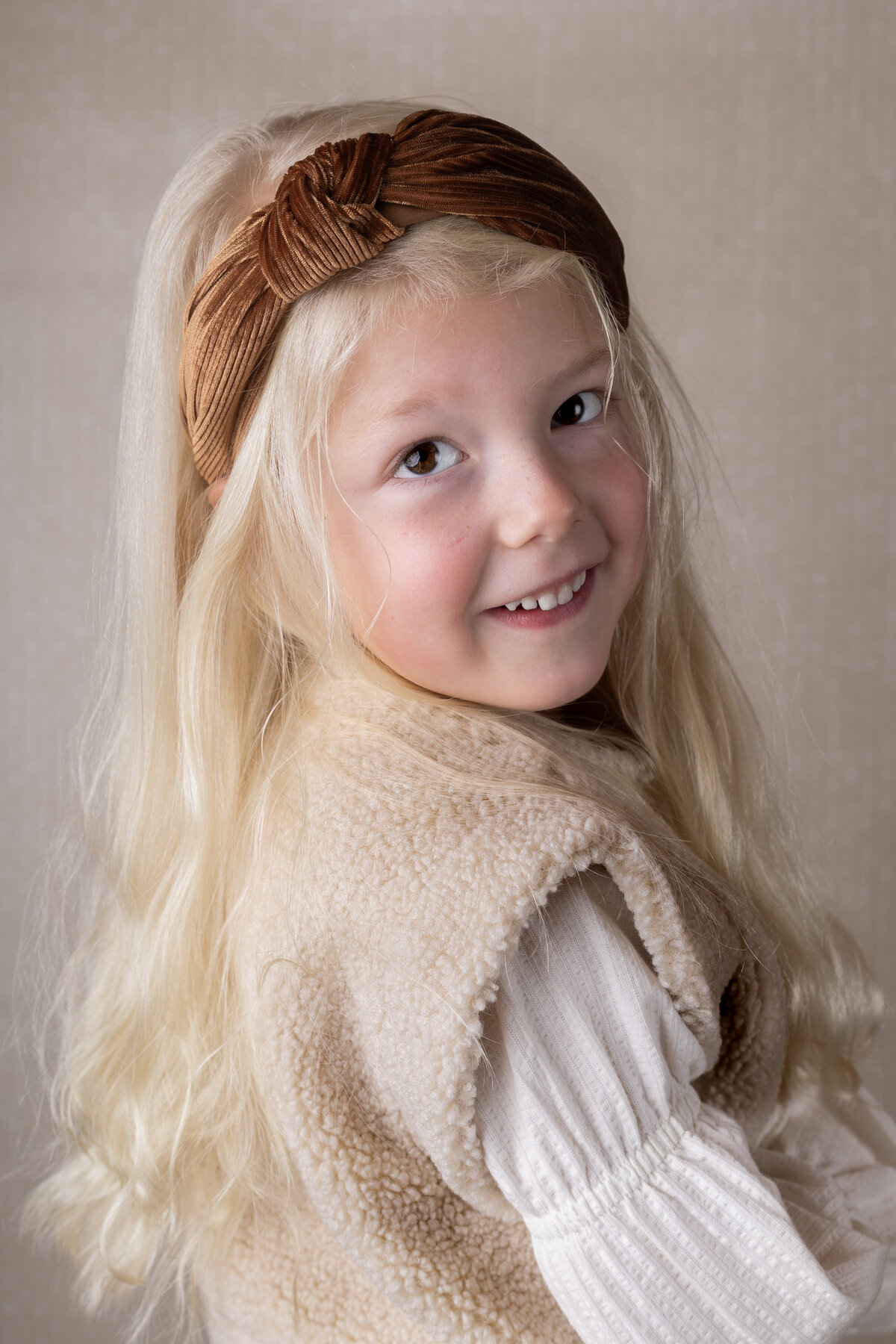Meisje van 4 met een creme kleurige achtergrond en roestbruine haarband in het haar tijdens een fotoshoot bij Evita Fotografie uit Zwartsluis