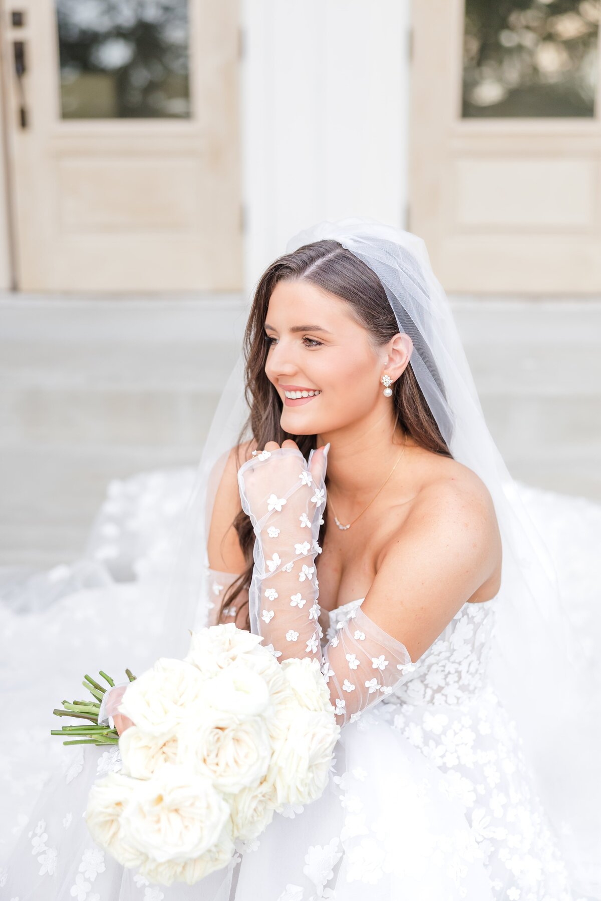An image from an Arkansas wedding photographer of a bride sitting on outdoor steps smiling with white bouquet