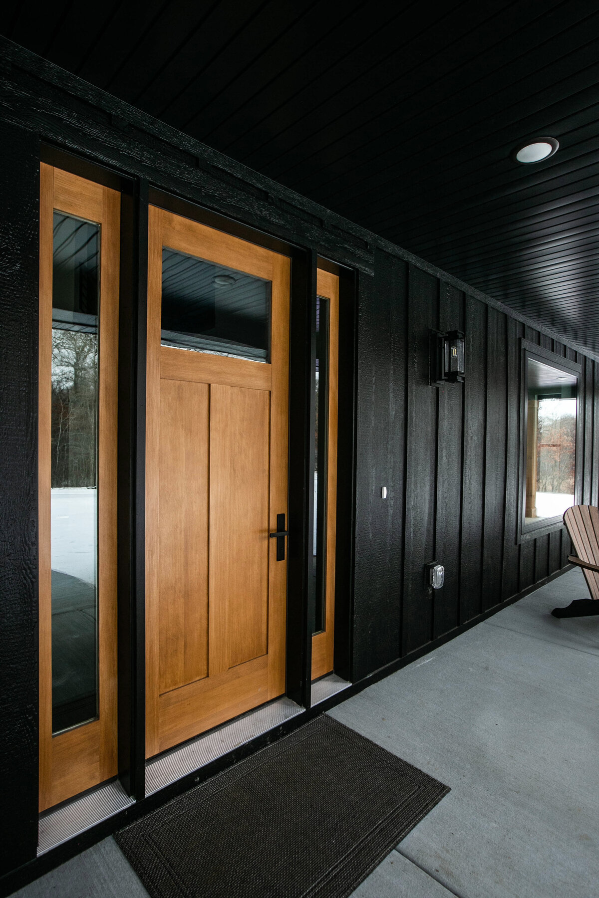 Exterior view of custom home in Elk River, Minnesota with black siding, wood details and front porch built by Cornerstone Custom Builds
