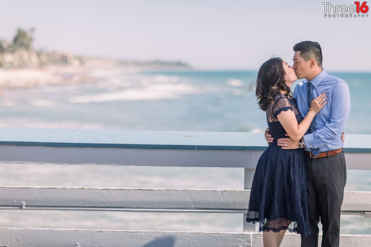 Engaged couple share a kiss while standing on the San Clemente Pier