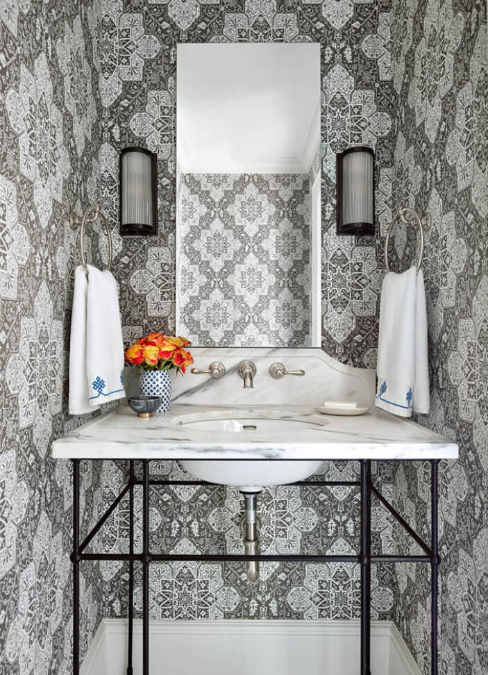 A powder room featuring Thibaut wallpaper, a Visual Comfort sconce, and a custom iron console with marble accents. Featured in Boston Home Magazine.