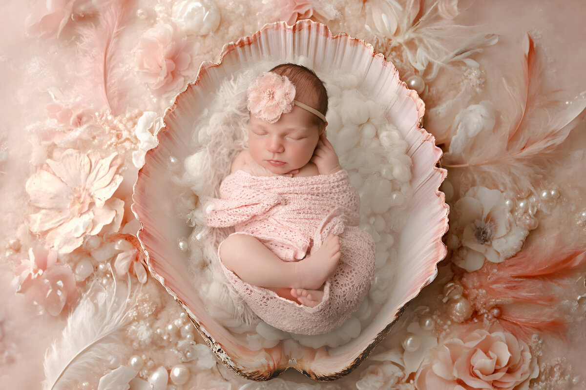 Baby sleeps surrounded by pink flowers and feathers