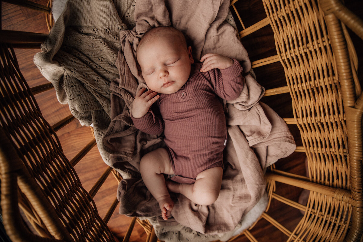 Newborn baby sleeps in cane bassinet during home newborn photography session