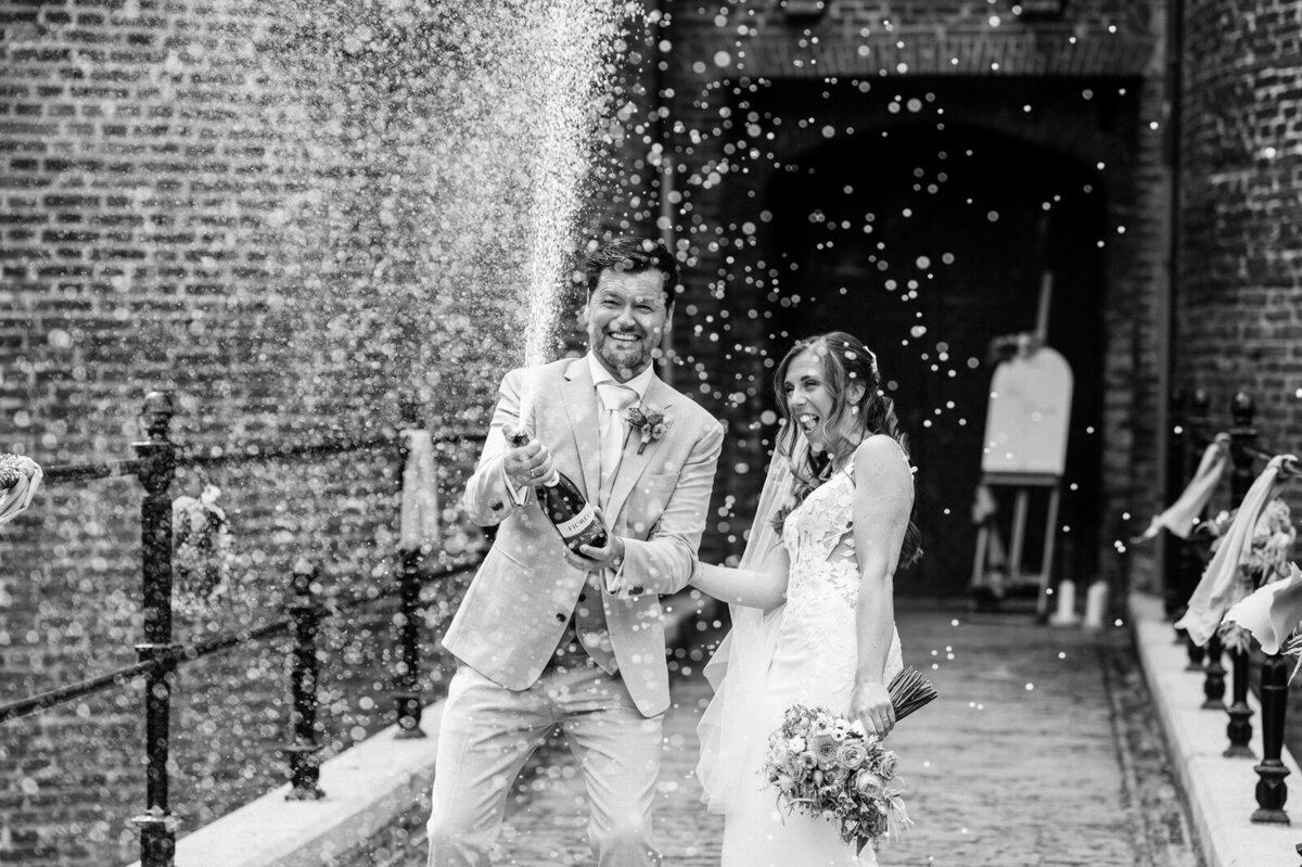 Bruidspaar ontpopt champagne en spuit die richting de trouwfotograaf