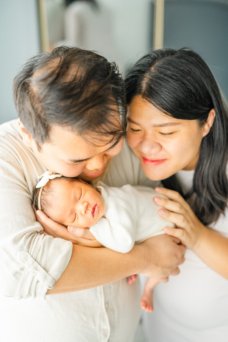 parents hold their infant baby girl while the father rests his head on her head during their lifestyle newborn session at their Austin home.