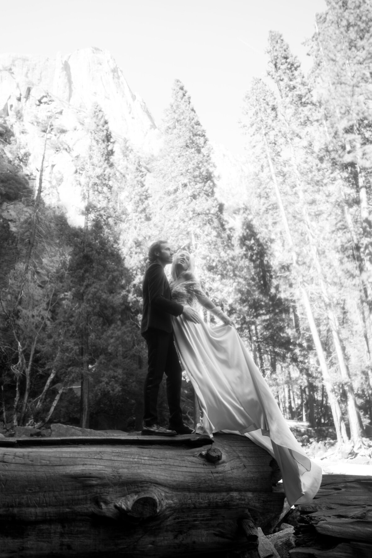 Bride and groom at Yosemite waterfall during golden hour embracing each other while the satin gown train flows in the back