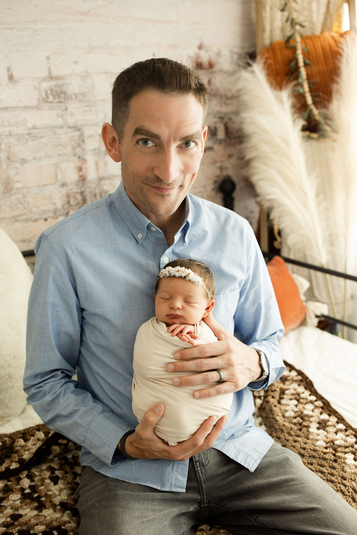 dad looking at the camera holding his newborn daughter proudly