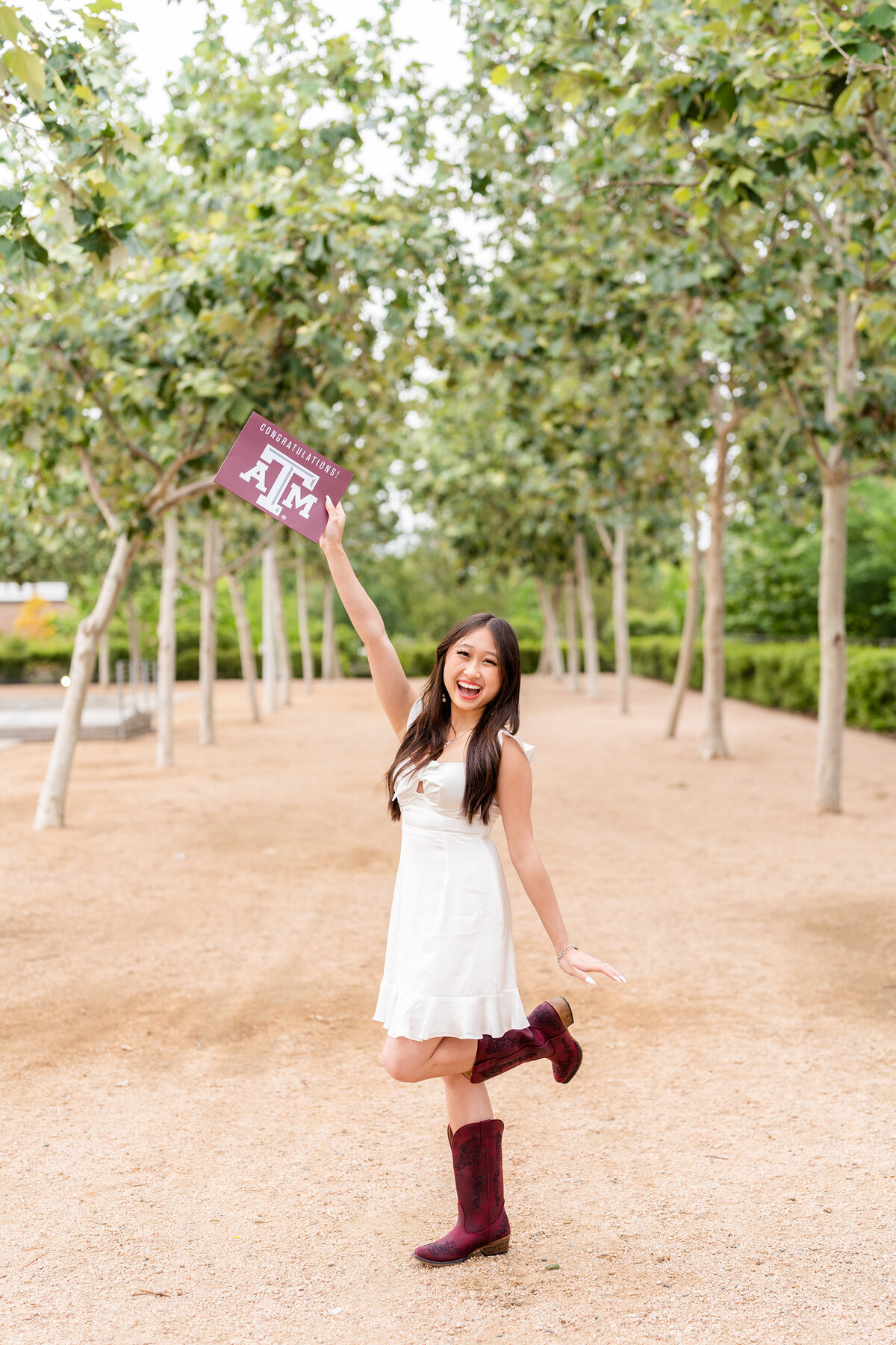 Houston high school senior holding up A&M acceptance letter and wearing white dress with maroon boots in Downtown Houston