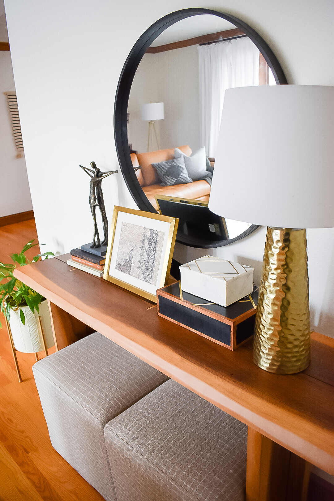 A black mirror hangs behind a wooden console table with a lamp